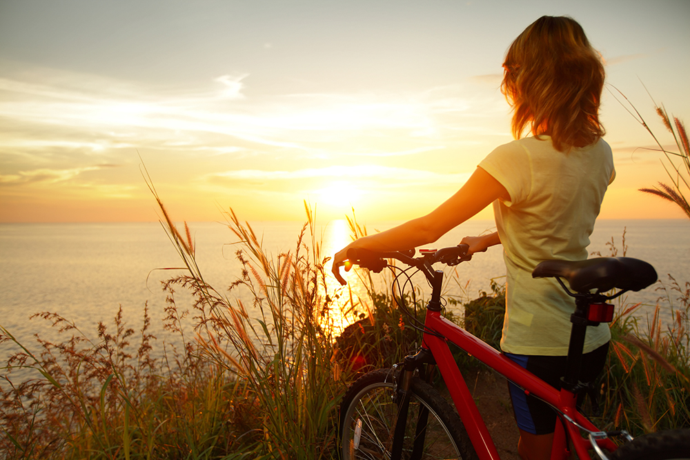 Person standing next to a bike watching the sun set